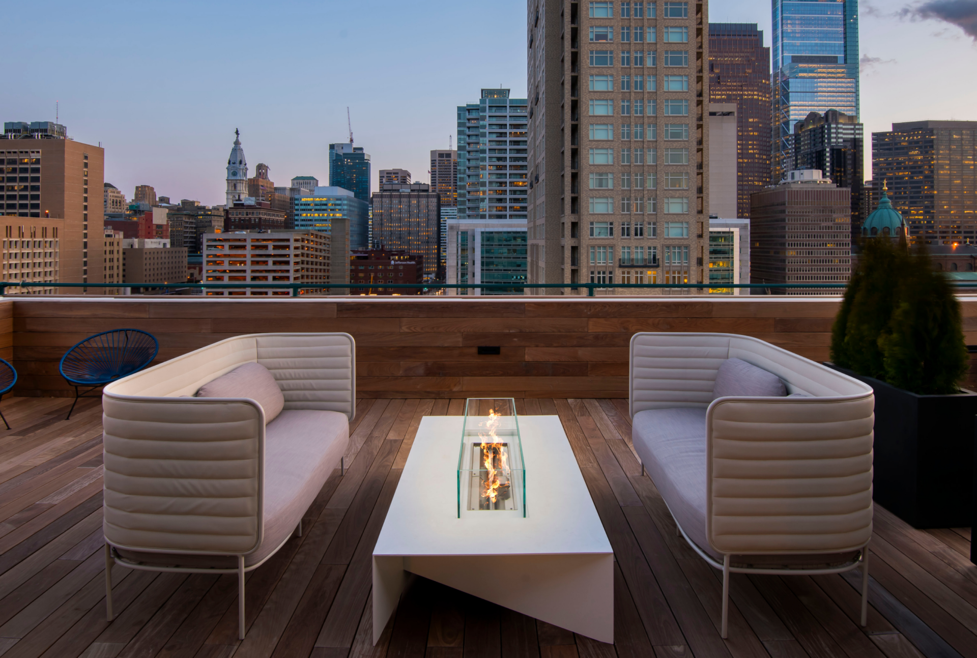 Rooftop lounge with sofas and a fire table overlooking the Philadelphia skyline at dusk.
