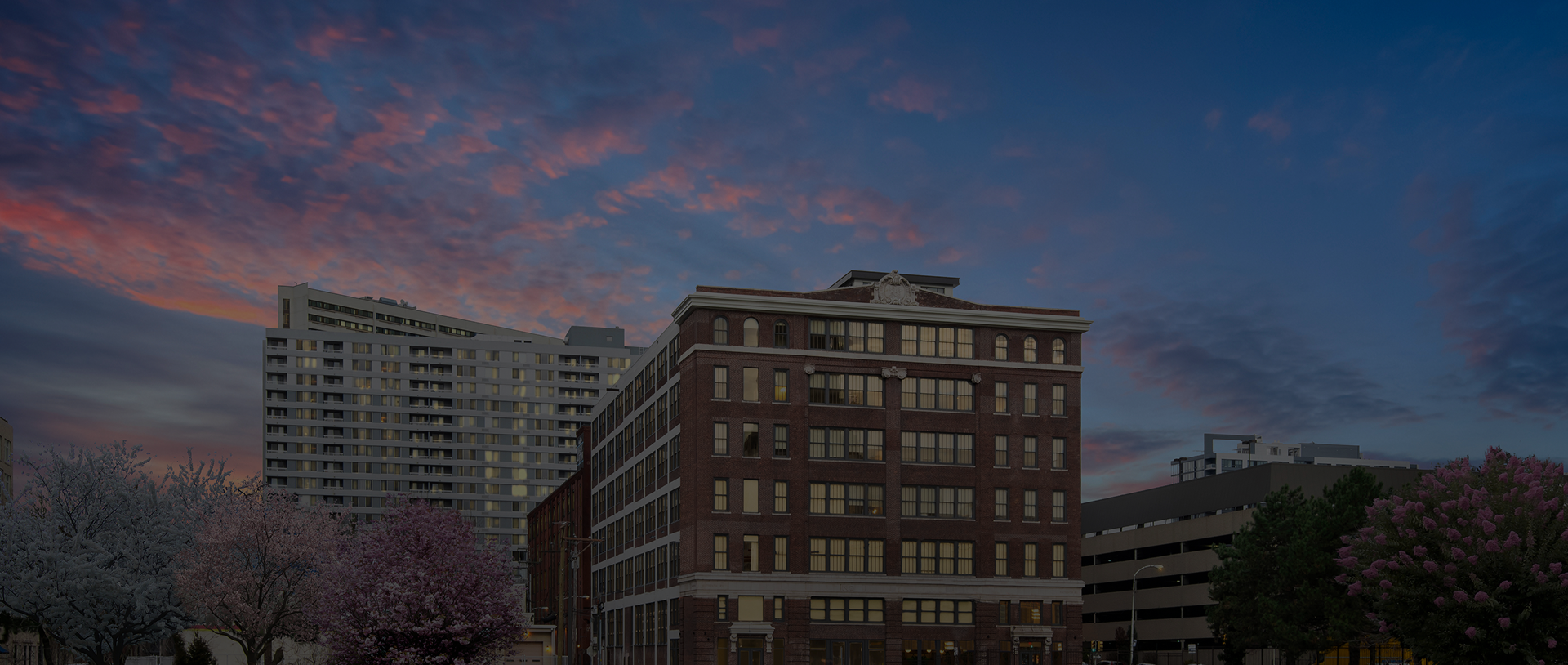 Historic brick building and surrounding city architecture beneath a dramatic sunset sky.