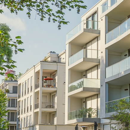 Modern residential building with glass balconies framed by leafy trees.
