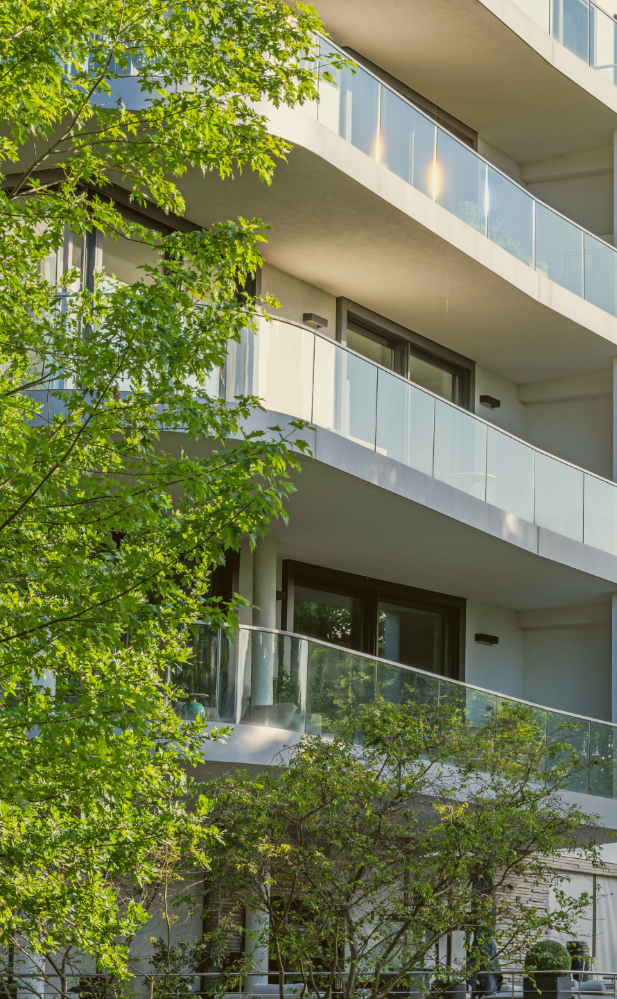 Modern residential building with curved glass balconies surrounded by lush green trees.