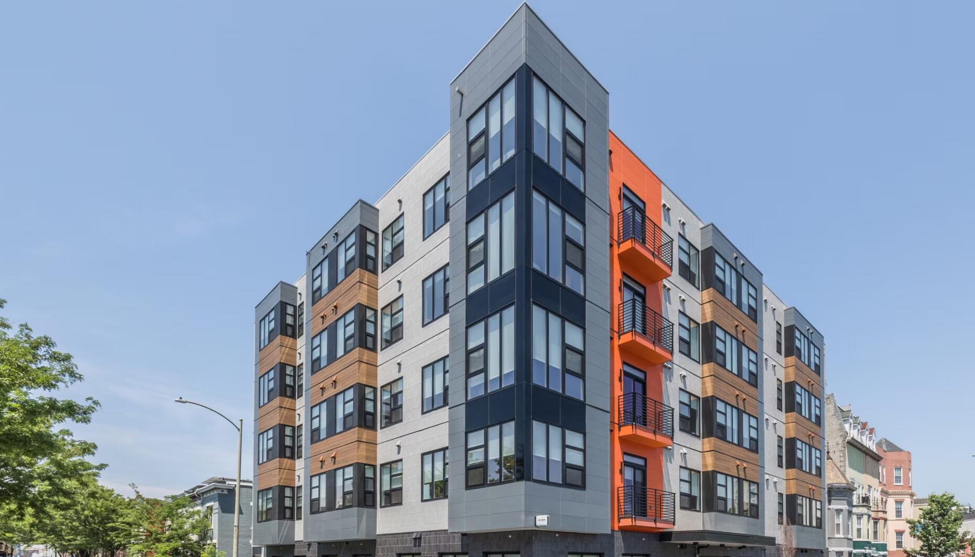 Modern multi-story residential building with gray, wood, and orange exterior accents.