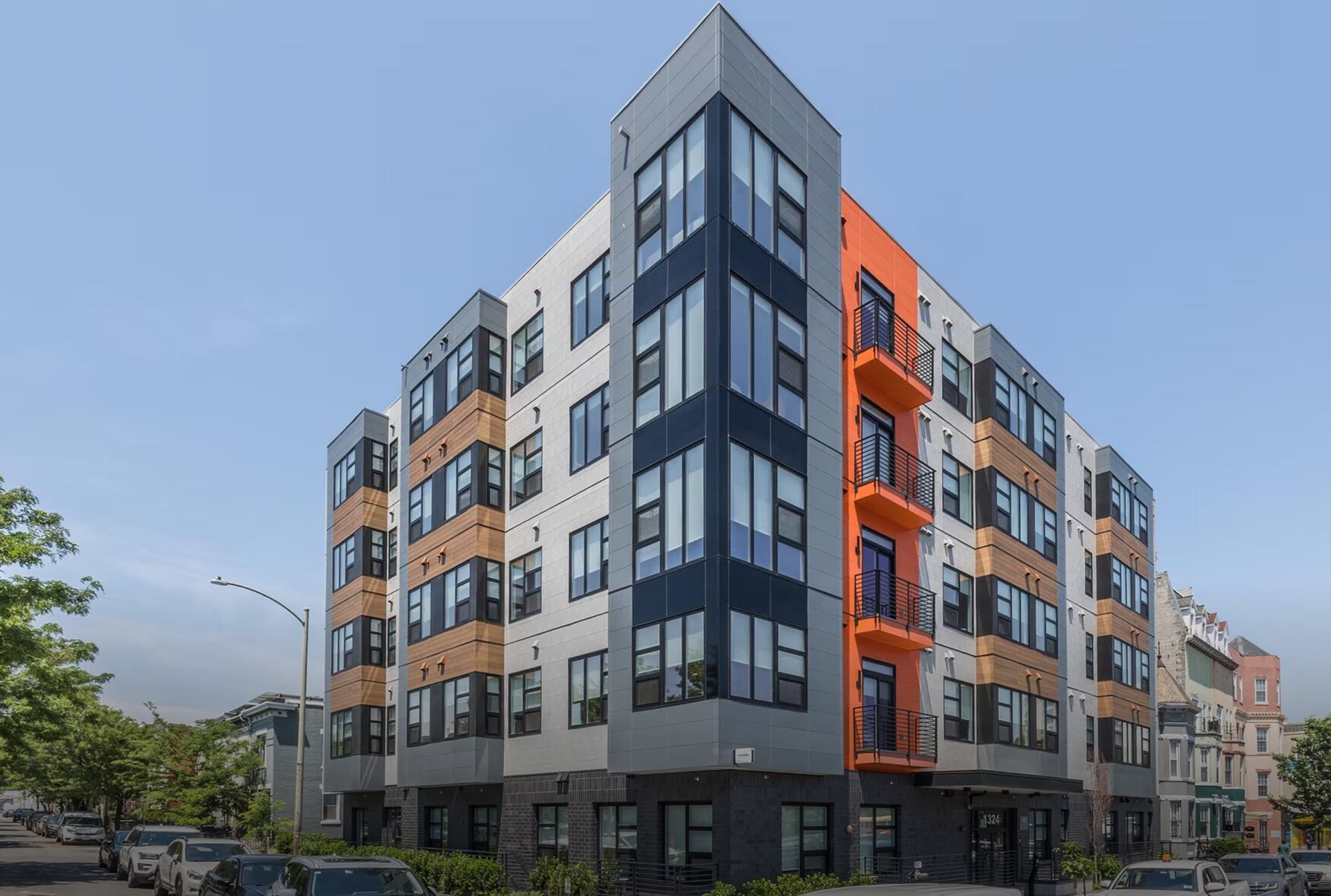 Modern multi-story residential building with gray, wood, and orange exterior accents.