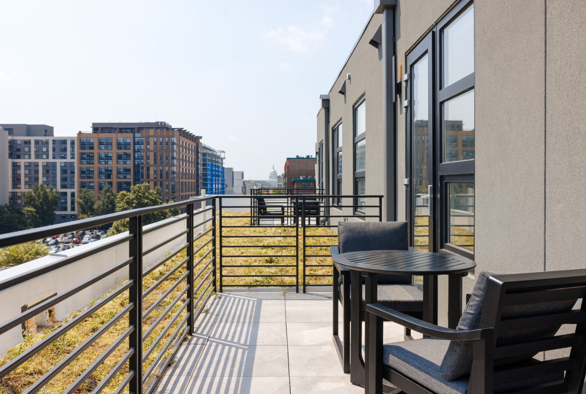 Private balcony with outdoor seating overlooking a modern urban neighborhood and city skyline.