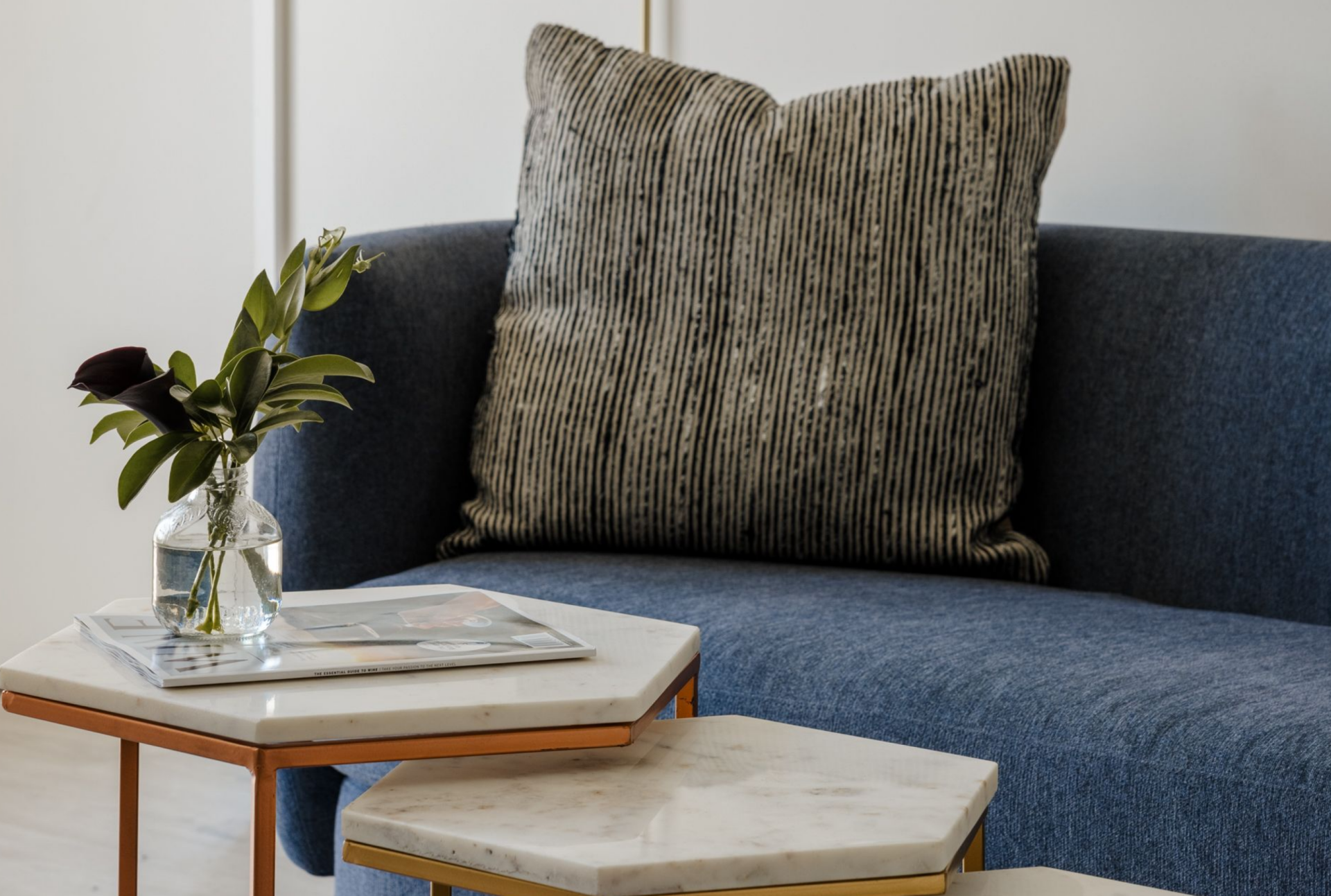 Blue upholstered armchair with a textured cushion beside marble-top nesting tables and a small floral arrangement.