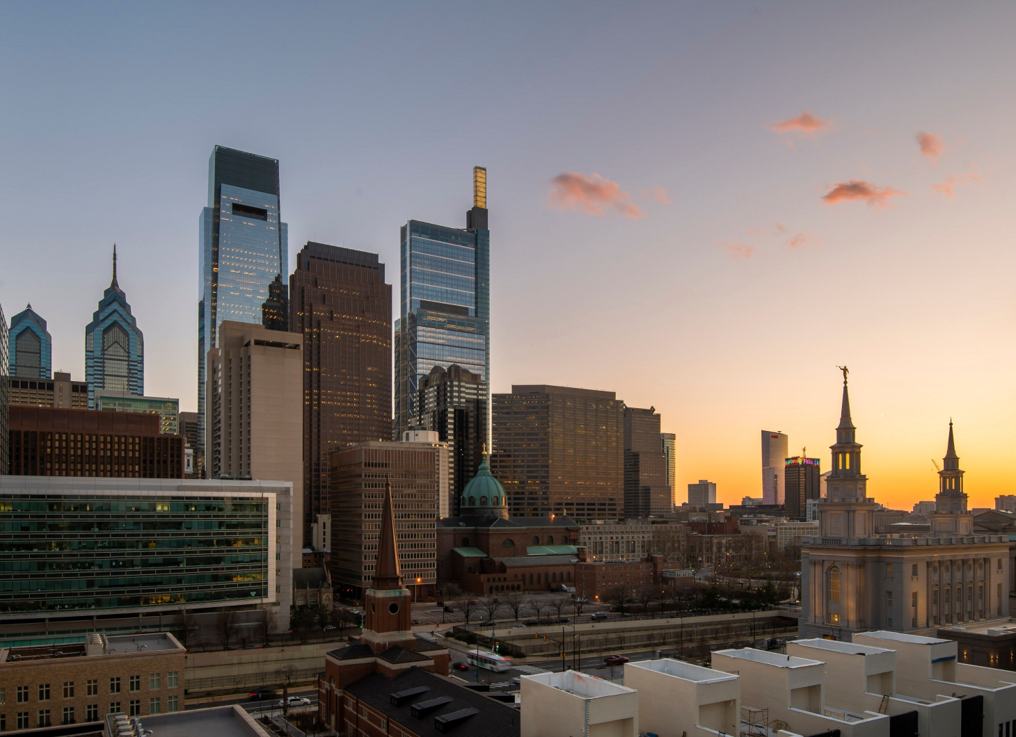 Philadelphia skyline at sunset with modern skyscrapers and historic church towers.