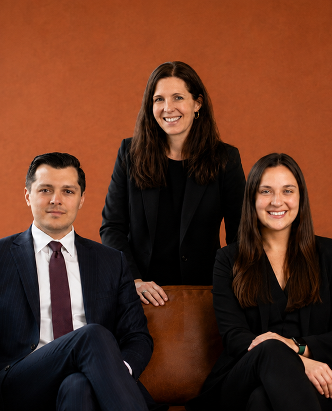Three professionals posing together in business attire against a warm orange background.