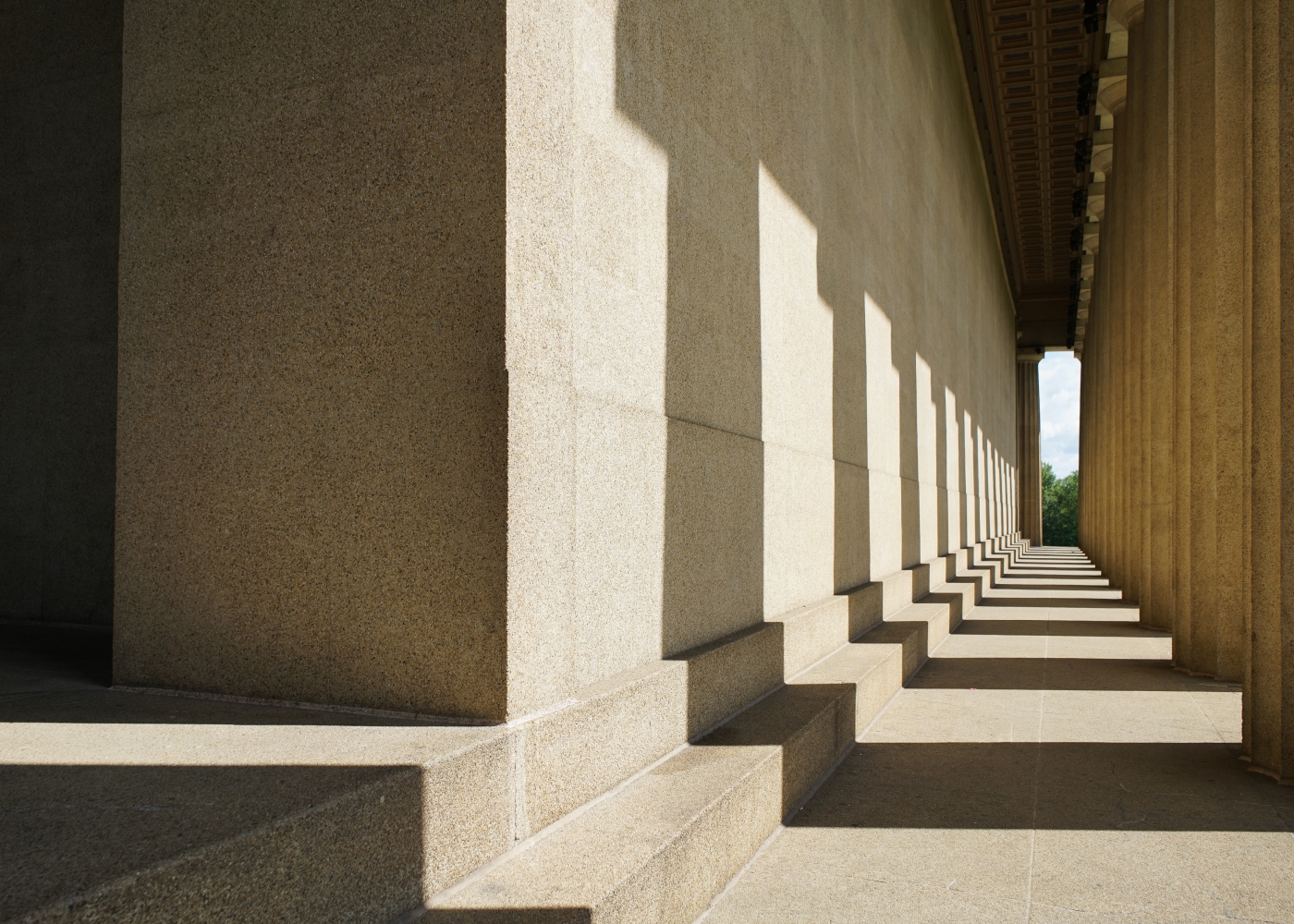 Sunlit stone colonnade with repeating columns and geometric shadows.
